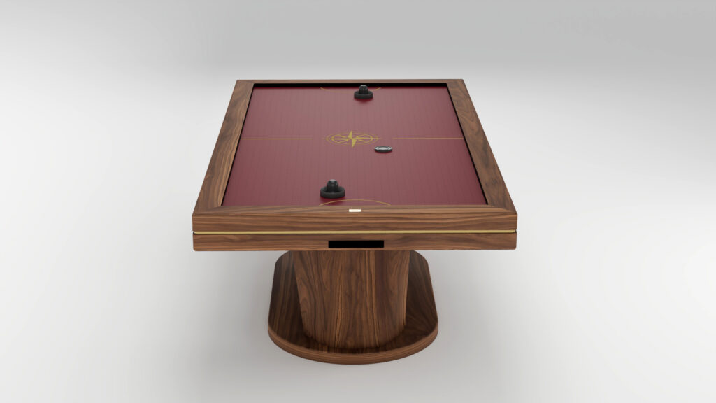 A handcrafted wooden air hockey table with a red playing surface, featuring two black strikers and a black puck. This luxury game table boasts a modern design and rests on a round wooden pedestal base.